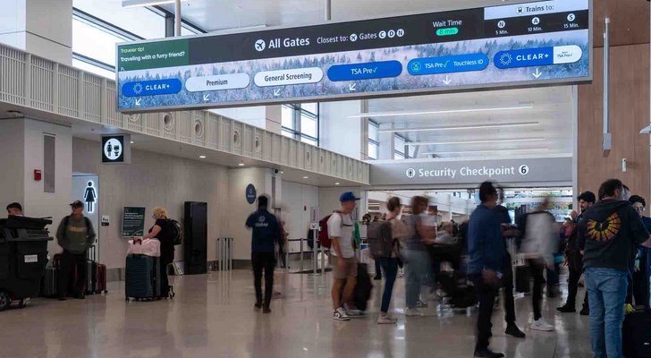 Airport security checkpoint with travelers beneath directional signage and screens