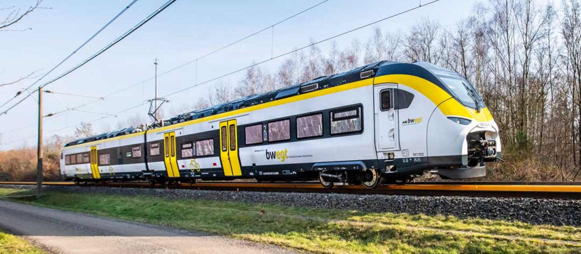 Modern regional train traveling through countryside with overhead electric lines