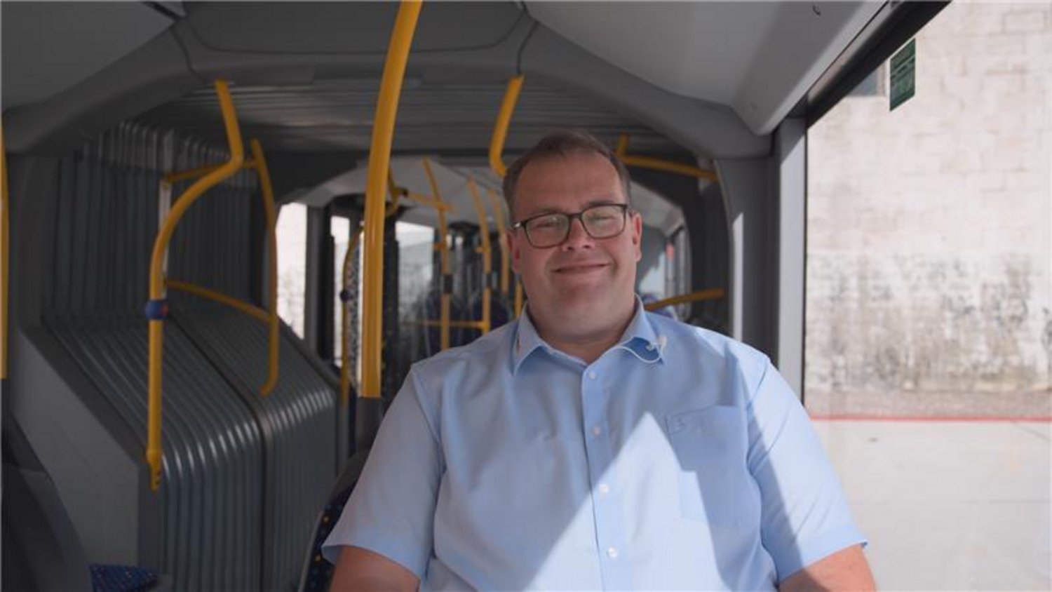 Man with glasses in light blue shirt sitting inside bus interior