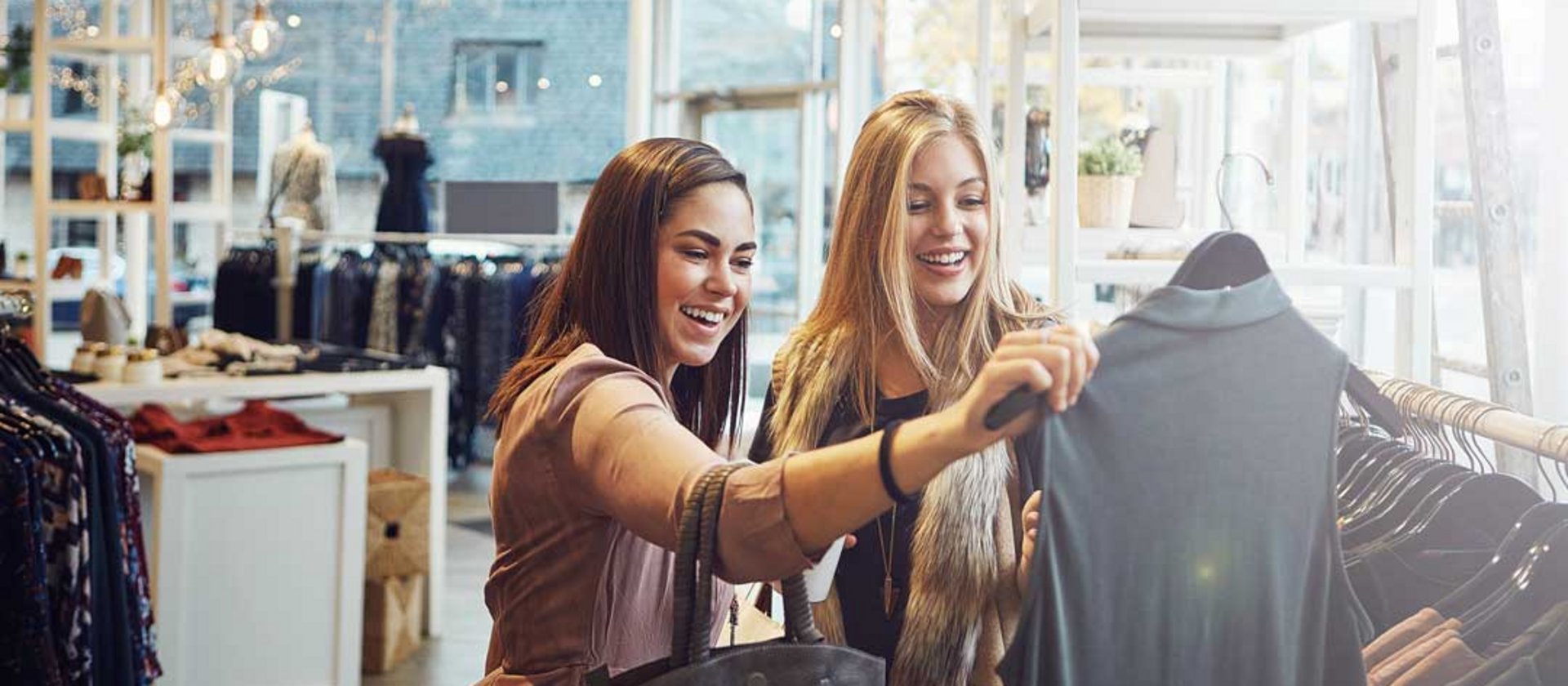 Two women shopping together, smiling while browsing clothes in retail store